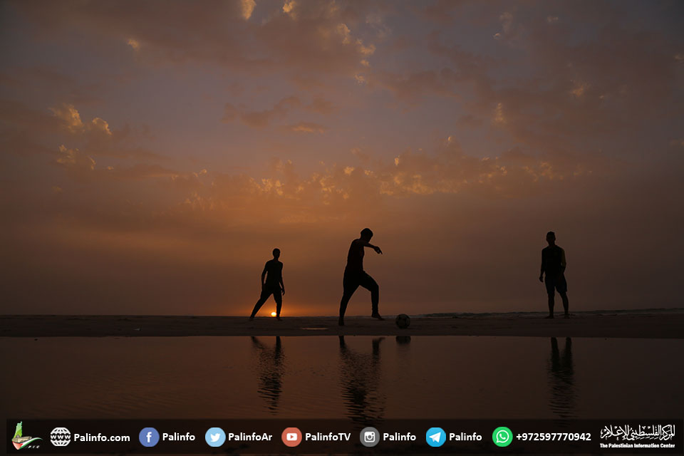 شبان يلعبون على شاطئ بحر غزة وقت غروب الشمس