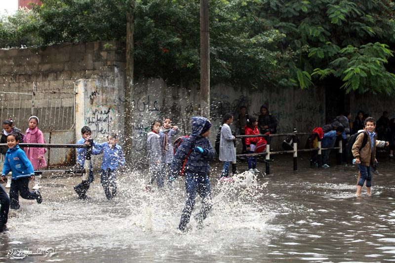 أطفال يلعبون ببركة مياه خلفتها الأمطار أمام بوابة مدرستهم